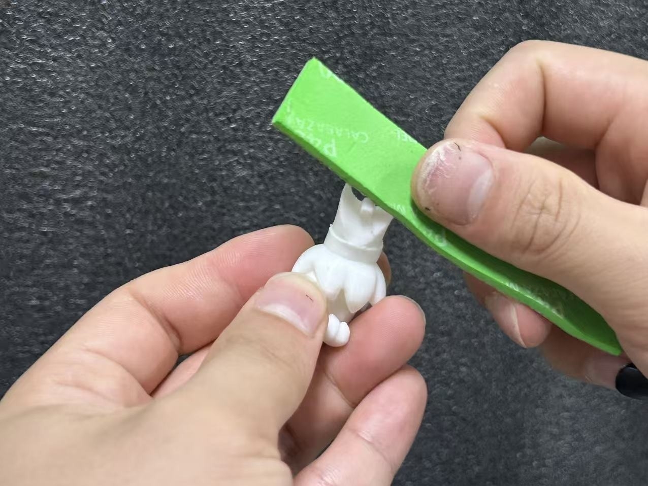 Sanding a resin 3D printed part to create a smooth assembly surface.